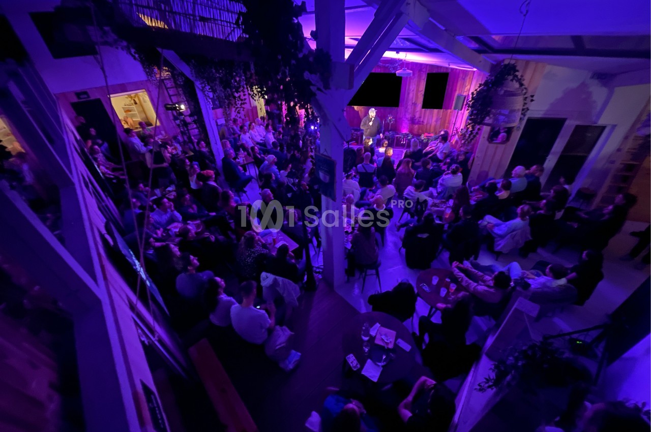 Salle comble éclairée de lumières violettes, avec un public attentif face à une scène où une personne s'exprime.