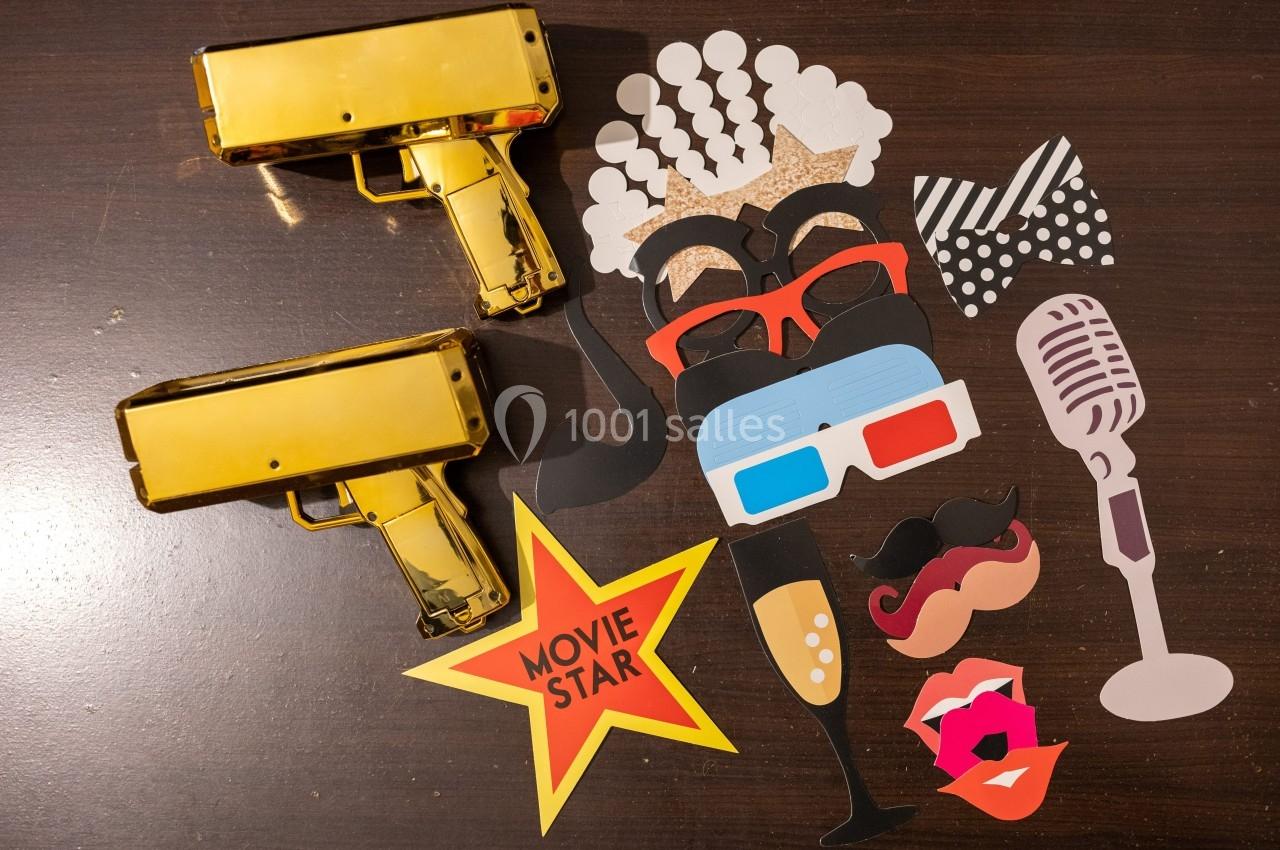 Accessoires de fête sur une table en bois, incluant lunettes, moustaches, micro, étoile ’Movie Star’ et pistolets dorés.