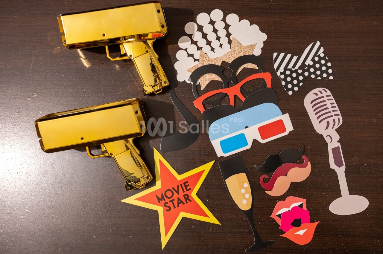 Accessoires de fête colorés sur une table en bois, incluant lunettes, moustaches, micro et pistolets dorés.