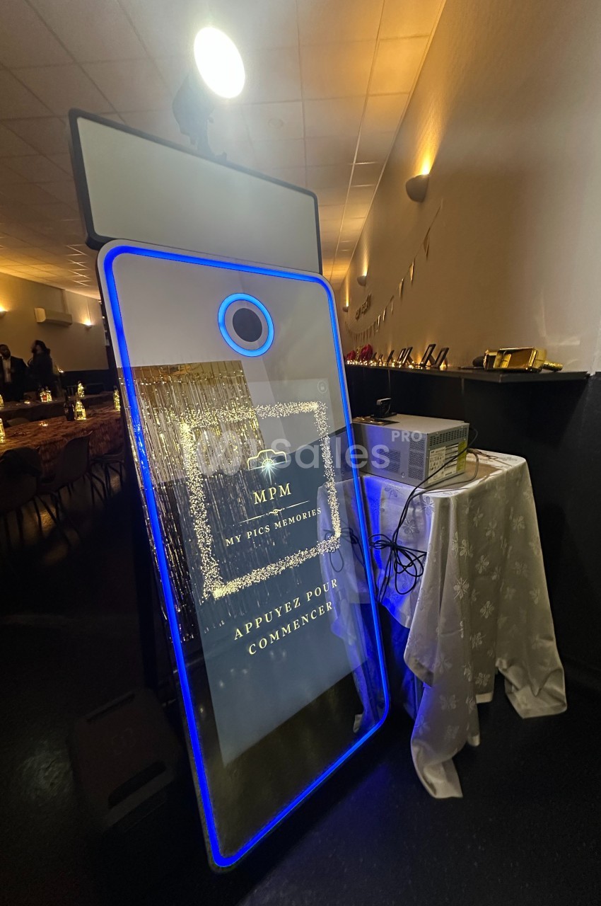 Borne photo interactive éclairée en bleu, installée dans une salle de réception avec des tables décorées en arrière-plan.