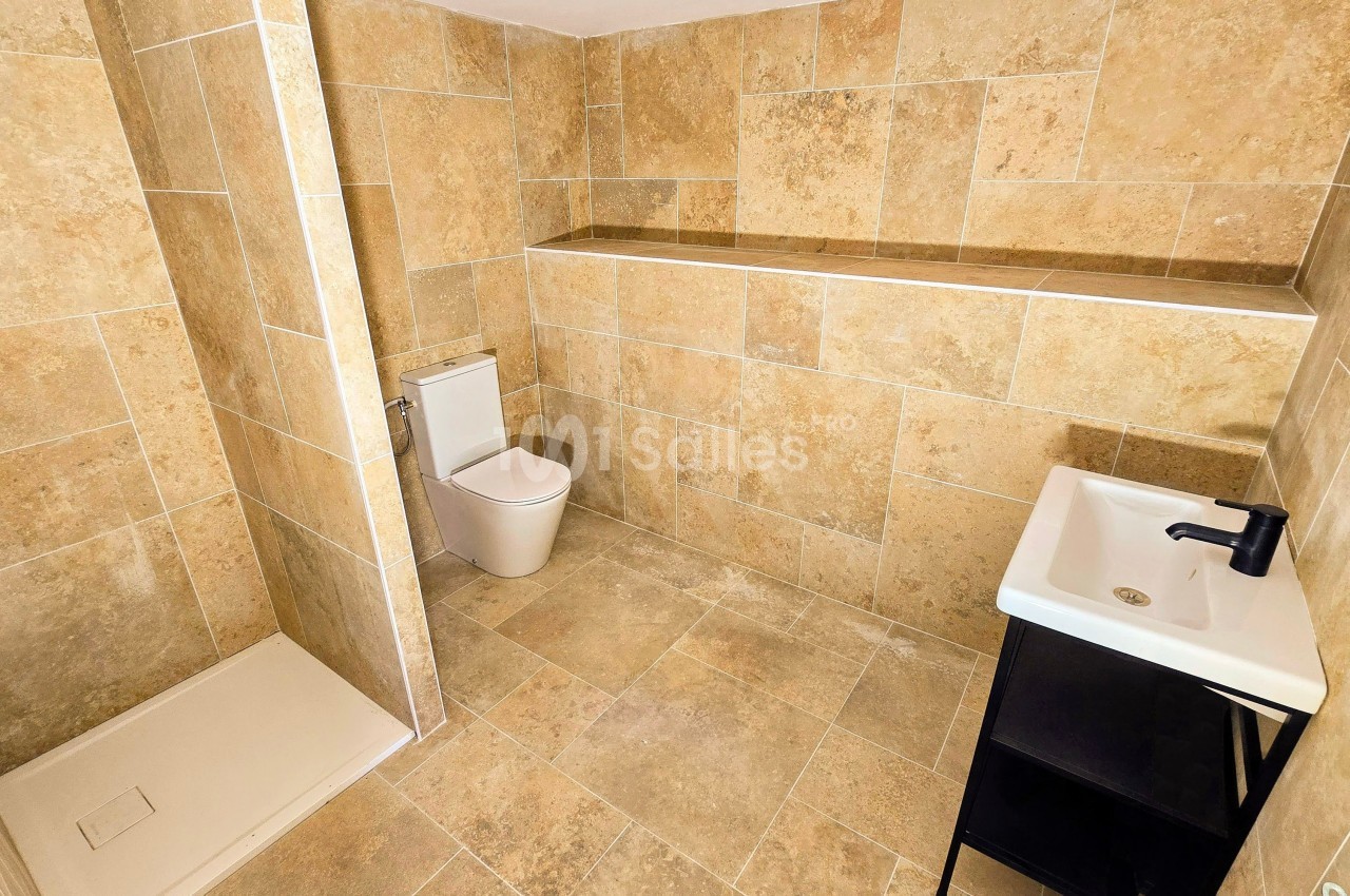 Salle de bain avec douche à l'italienne, toilettes modernes, lavabo sur meuble noir et murs en carrelage beige.