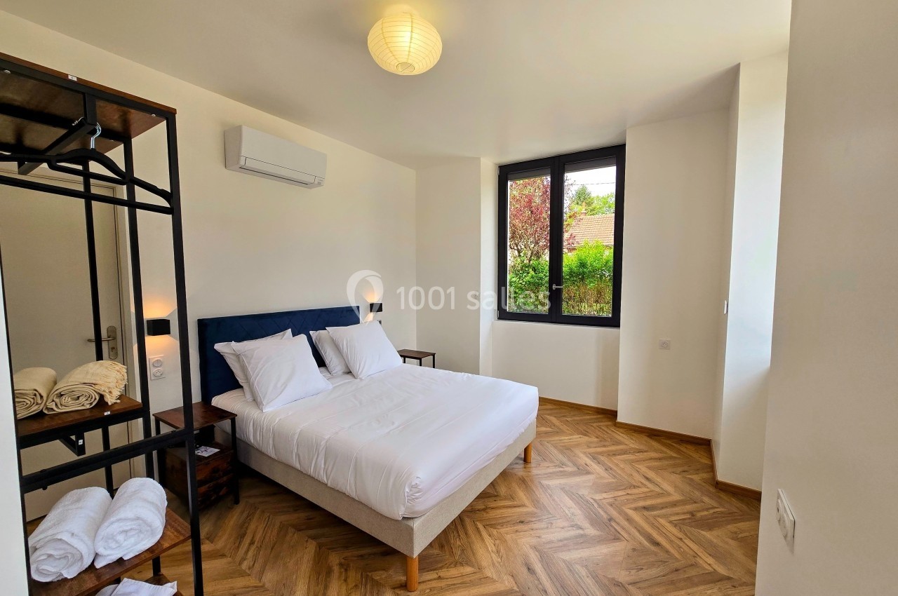 Chambre lumineuse avec lit double, parquet en chevrons, étagère métallique et fenêtre donnant sur un jardin.