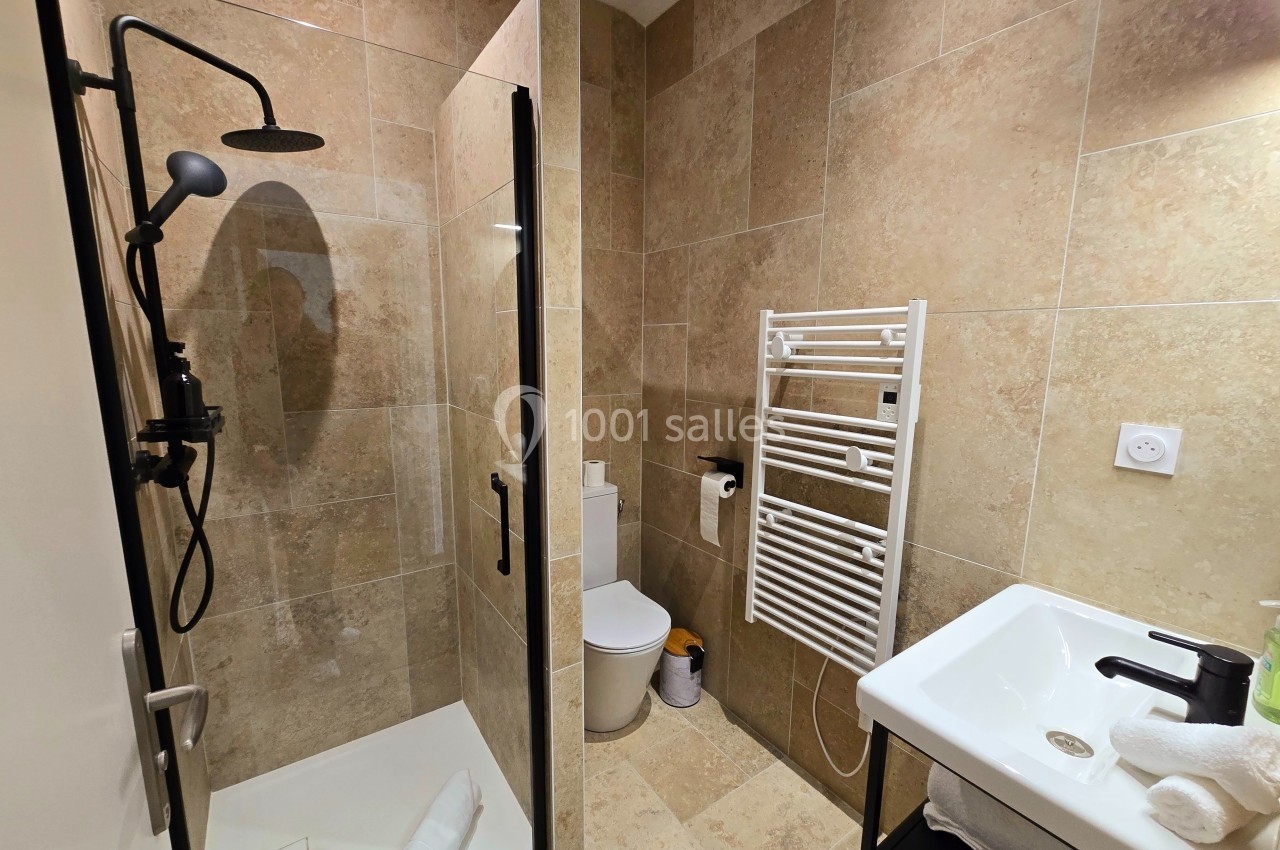 Salle de bain moderne avec douche à l'italienne, carrelage beige, lavabo, toilettes et sèche-serviettes mural.