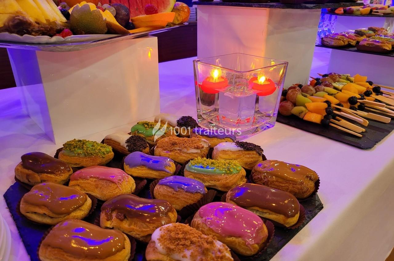 Plateau d'éclairs colorés, fruits frais et bougies décoratives sur une table de buffet.