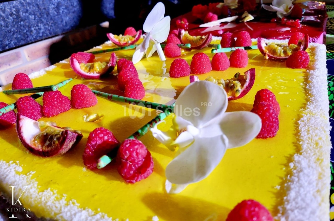 Gâteau décoré de framboises, fleurs en sucre et fruits de la passion sur un glaçage jaune vif.