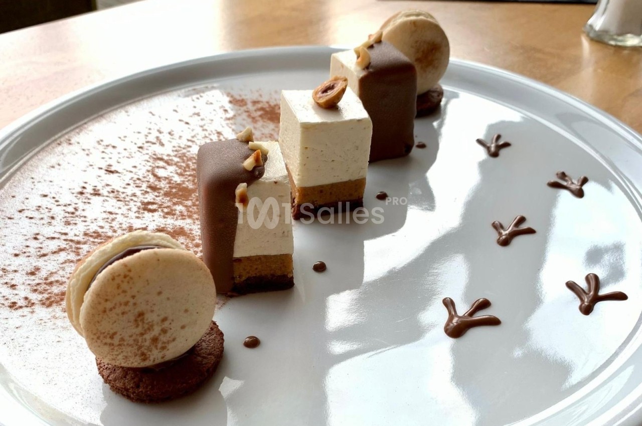 Dessert raffiné composé de mousses, macarons, chocolat et décorations en cacao sur une assiette blanche.
