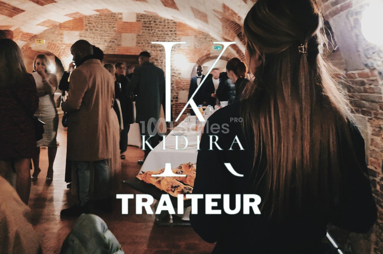 Des convives discutent dans une salle voûtée en briques, avec un buffet visible au premier plan.