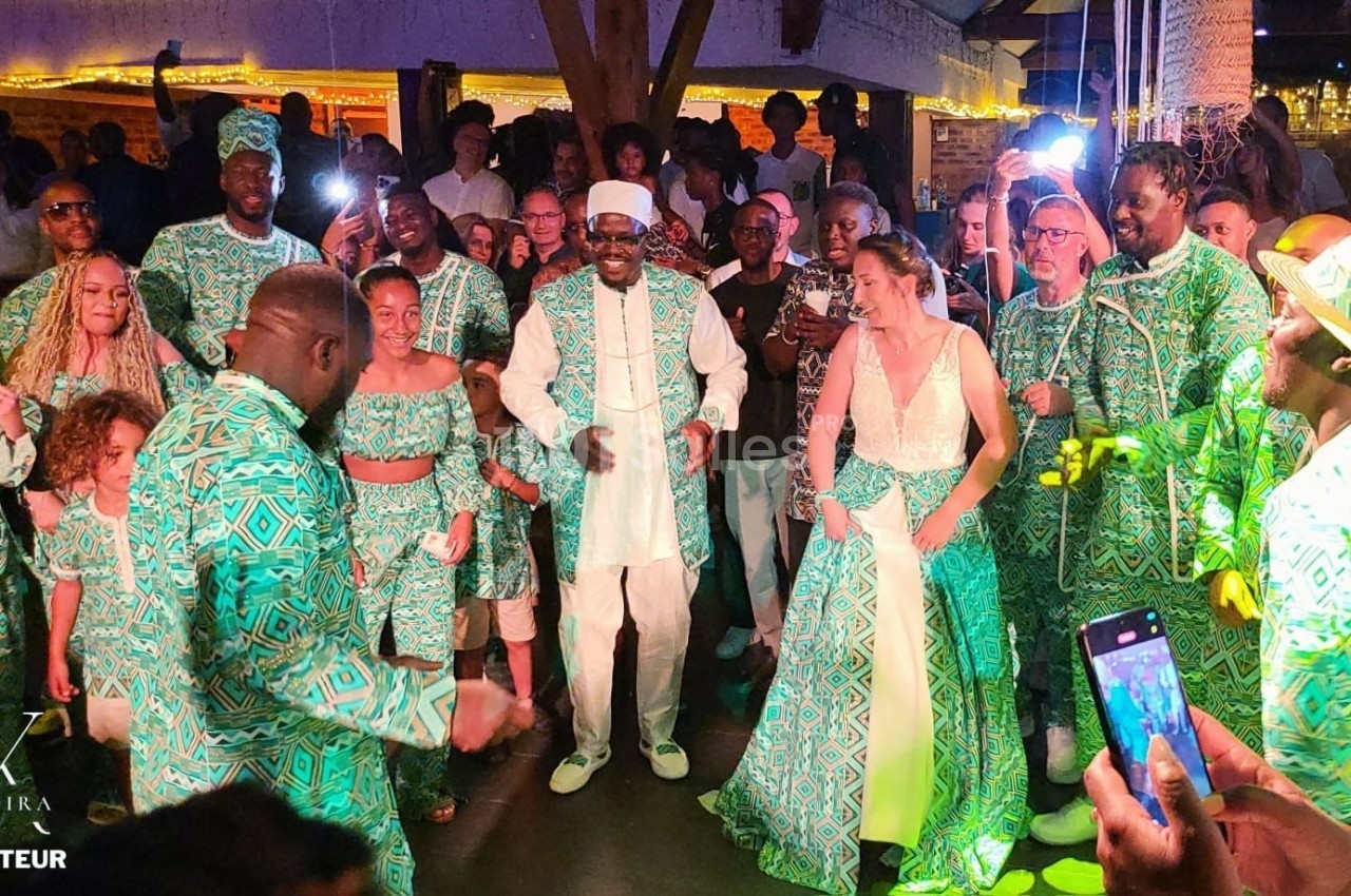 Groupe de personnes dansant lors d'une fête, habillées en tenues traditionnelles vertes et blanches.
