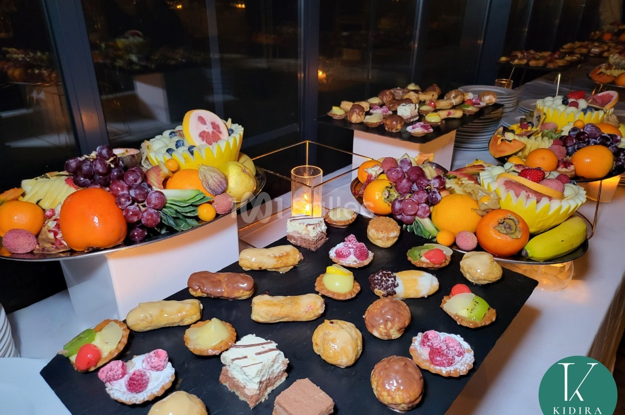 Plateau de desserts variés avec pâtisseries, fruits frais et décorations, disposé sur une table lors d'un buffet.
