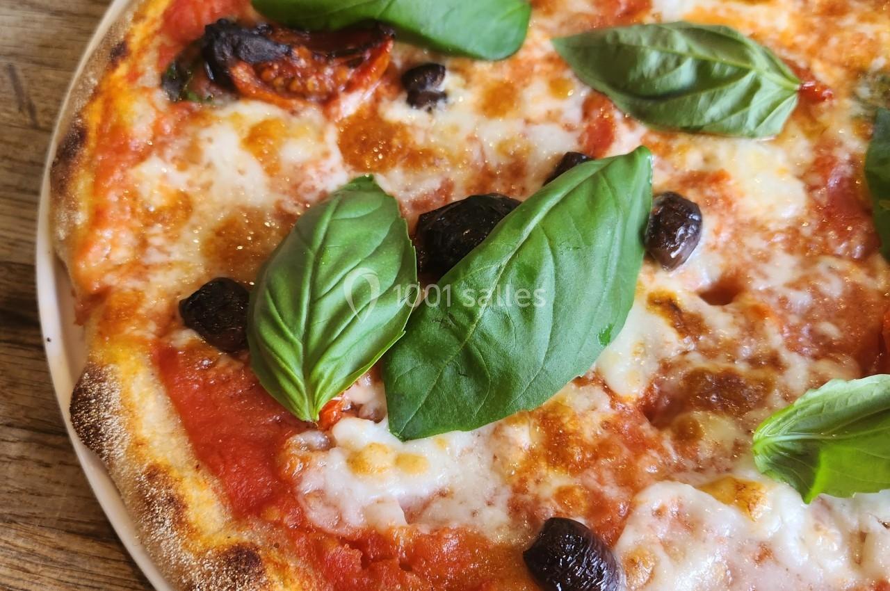 Pizza margherita garnie de feuilles de basilic frais, olives noires et fromage fondu sur une pâte dorée.