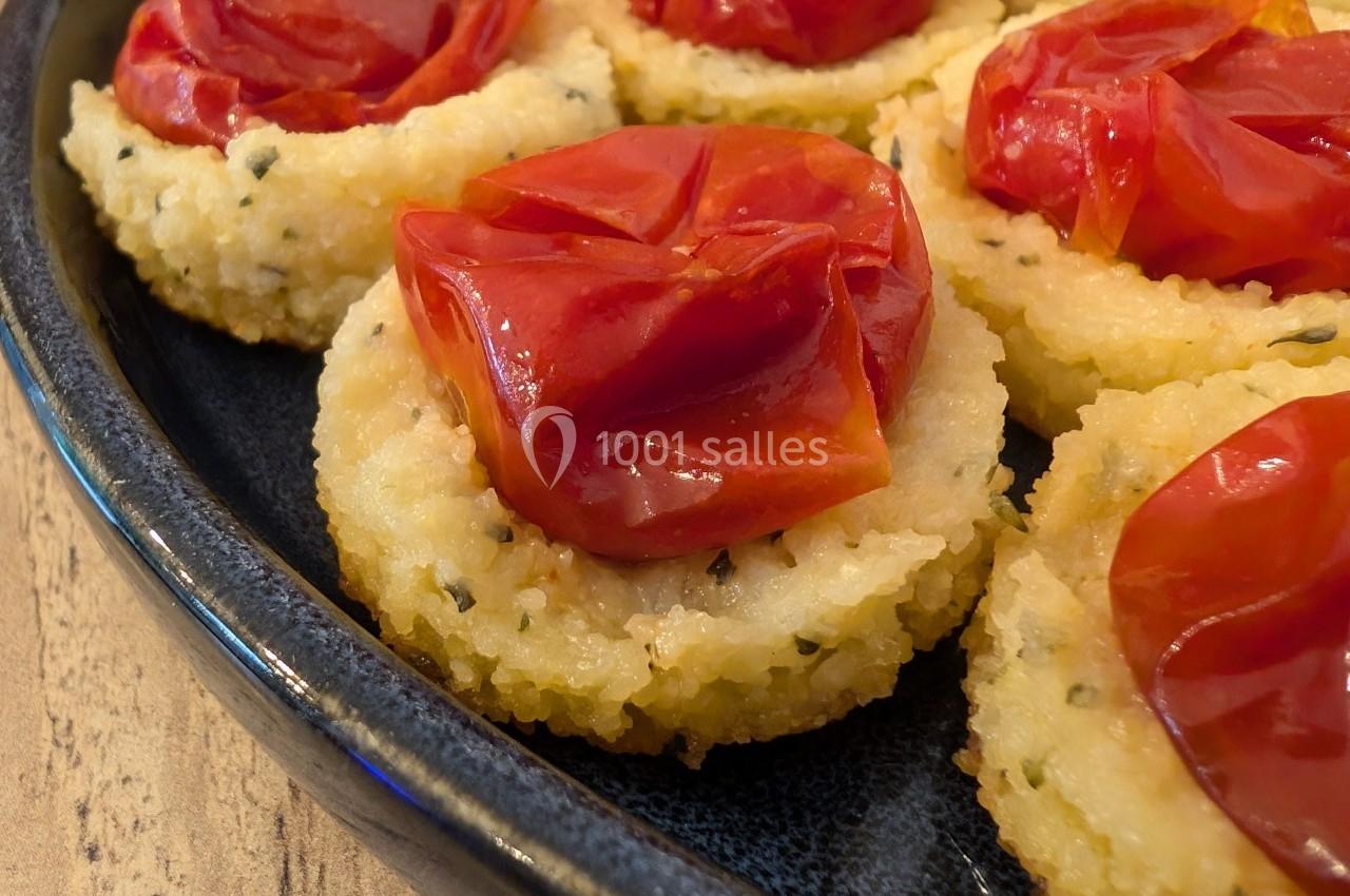 Assiette de bouchées de polenta garnies de tomates cerises rôties, présentées sur une table en bois.