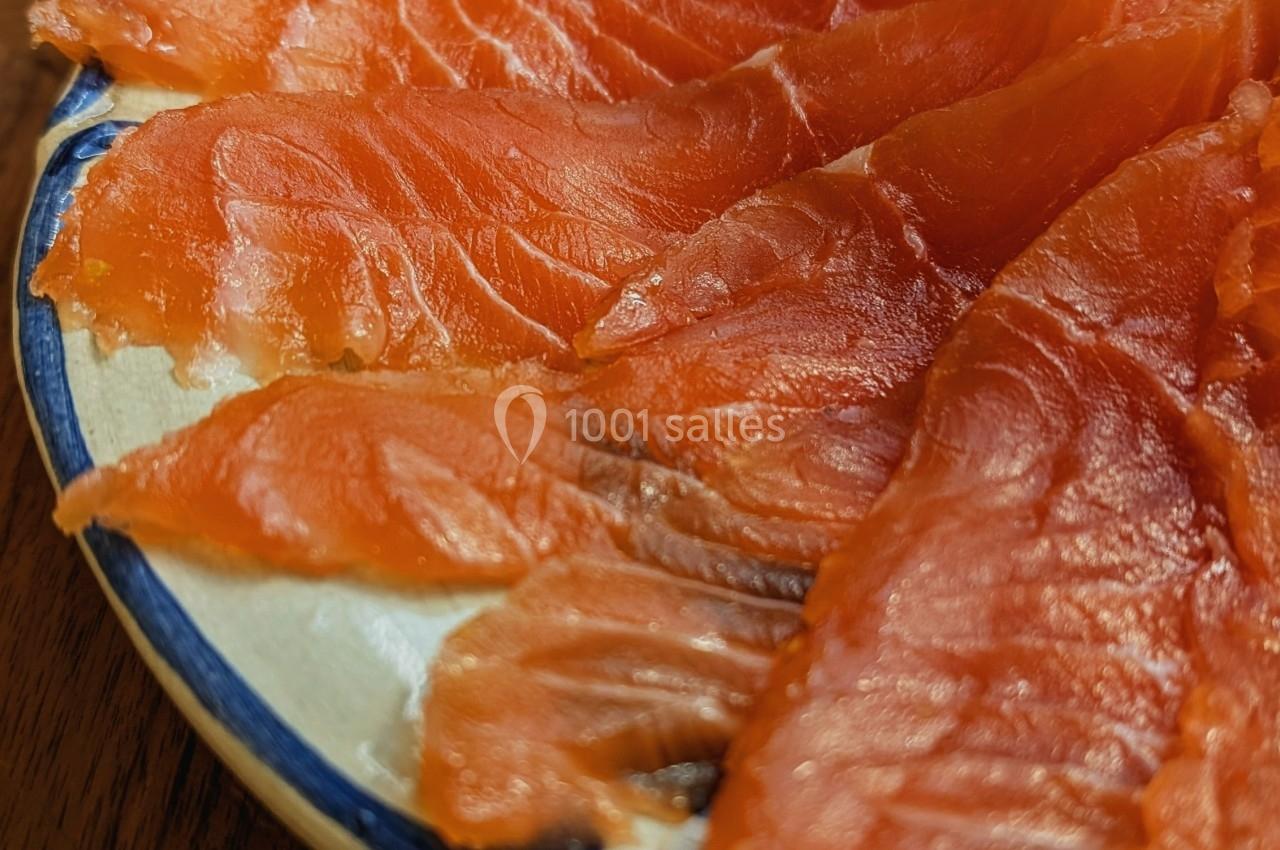 Tranches de saumon fumé disposées en éventail sur une assiette blanche bordée de bleu, posée sur une table en bois.