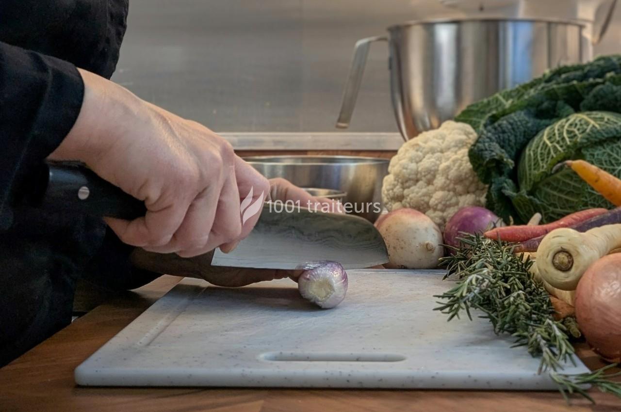 Une personne coupe un oignon sur une planche en bois, entourée de légumes frais et d'herbes aromatiques.