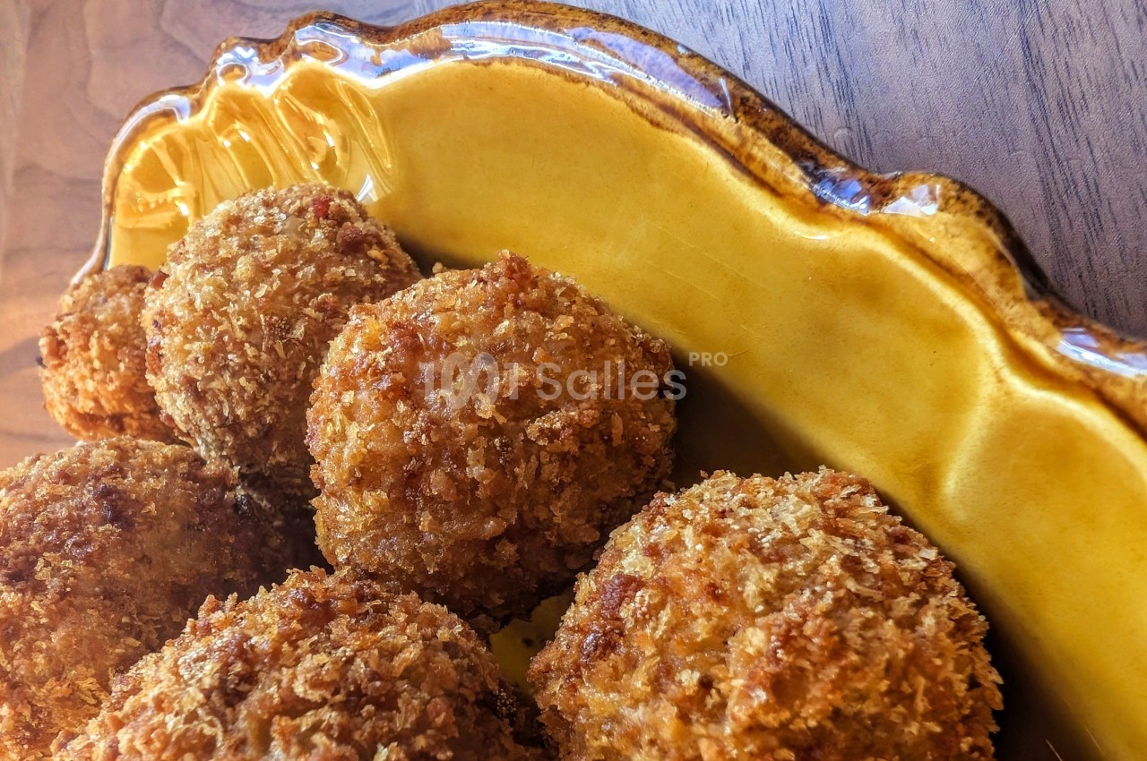 Boulettes panées dorées servies dans un plat en céramique jaune sur une table en bois.