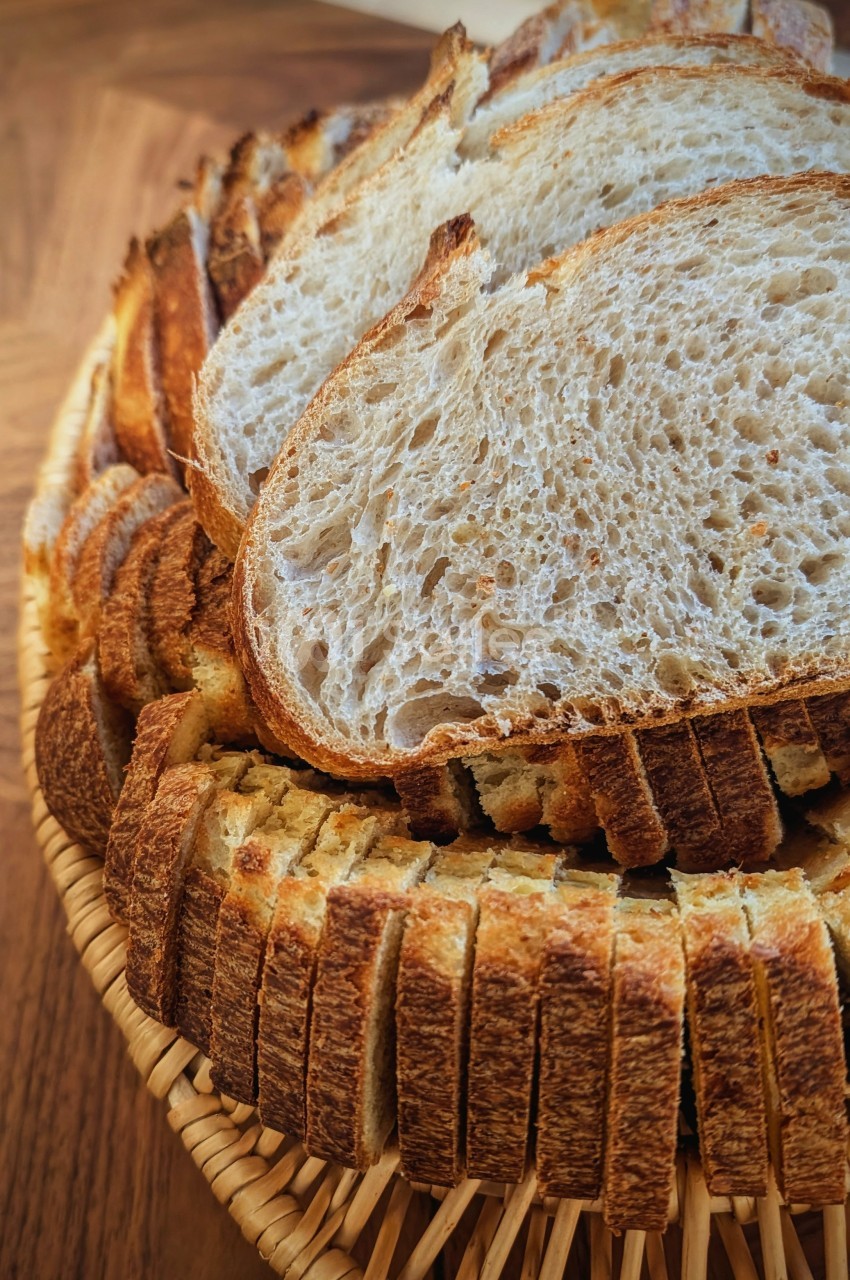 Tranches de pain artisanal disposées en éventail dans un panier en osier sur une table en bois.