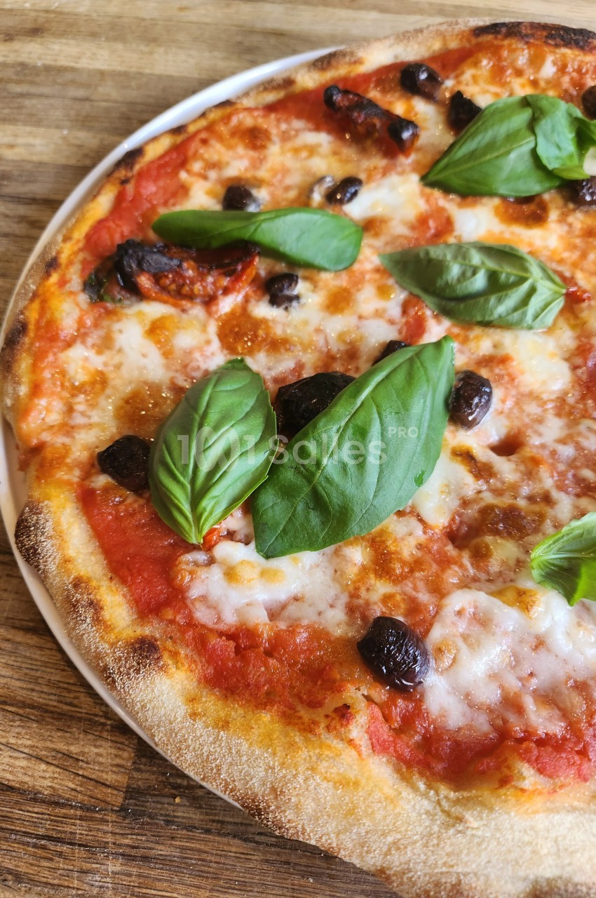 Pizza margherita garnie de feuilles de basilic frais, olives noires et fromage fondu sur une pâte dorée.