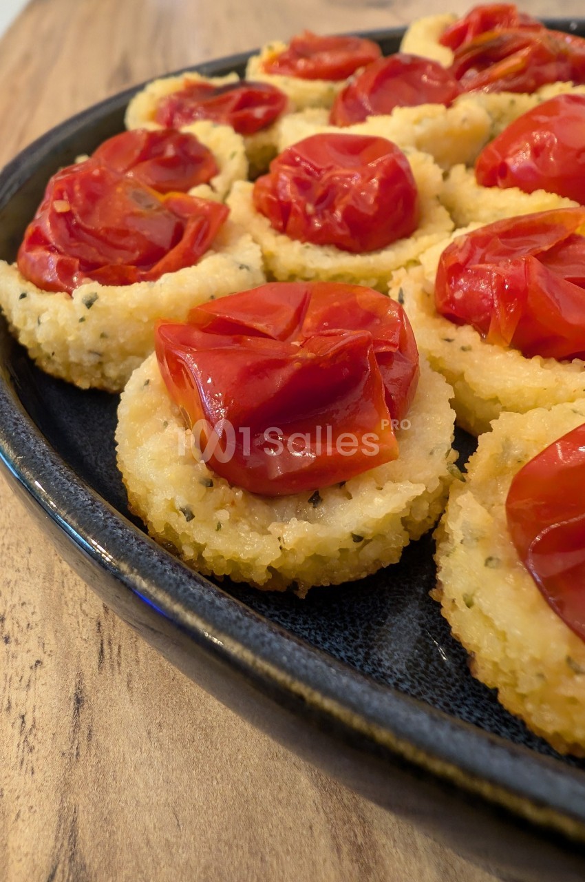 Assiette de bouchées de polenta garnies de tomates cerises rôties, présentées sur une table en bois.