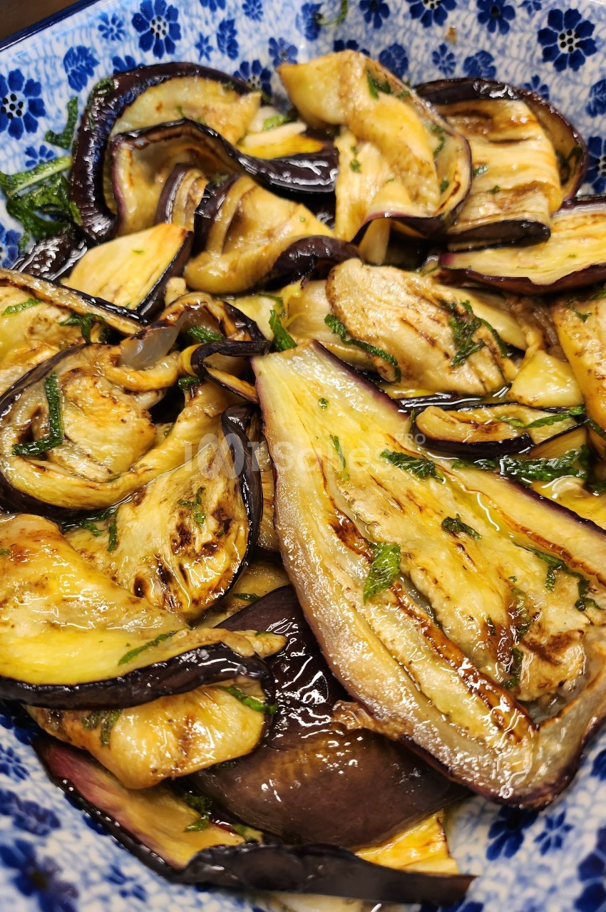 Tranches d'aubergines grillées assaisonnées avec des herbes fraîches, servies dans un plat à motifs bleus.