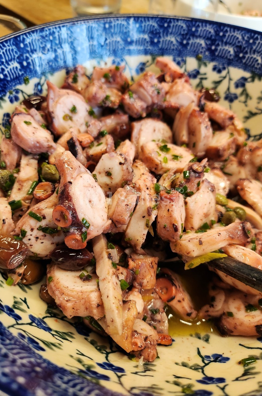 Salade de poulpe assaisonnée avec des herbes fraîches, servie dans un bol en céramique décoré de motifs bleus.