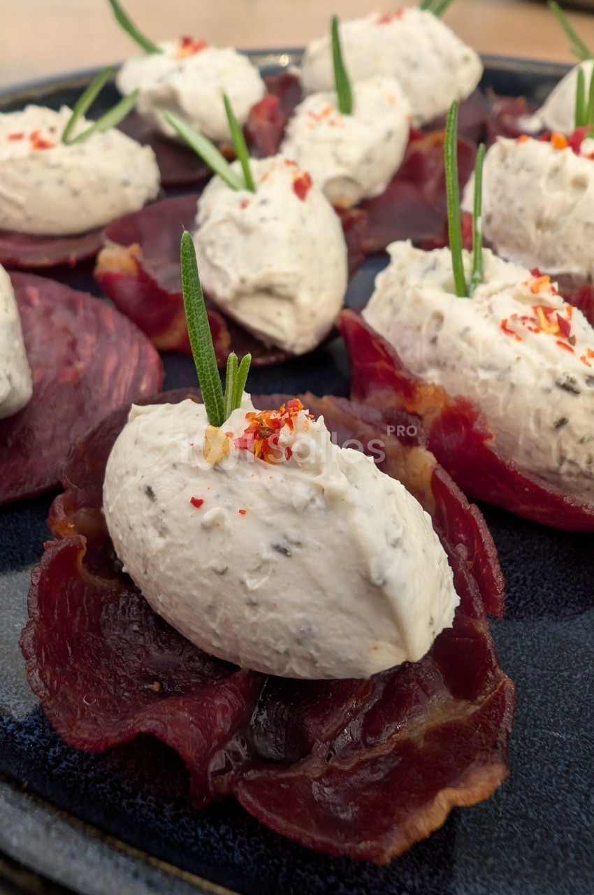 Tranches de viande séchée garnies de quenelles de fromage frais, décorées de brins de romarin et de piment.