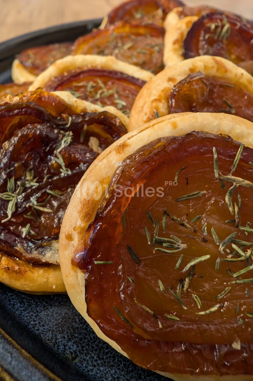 Tartelettes fines garnies de tranches de tomates caramélisées et saupoudrées d'herbes aromatiques, servies sur une assiette.