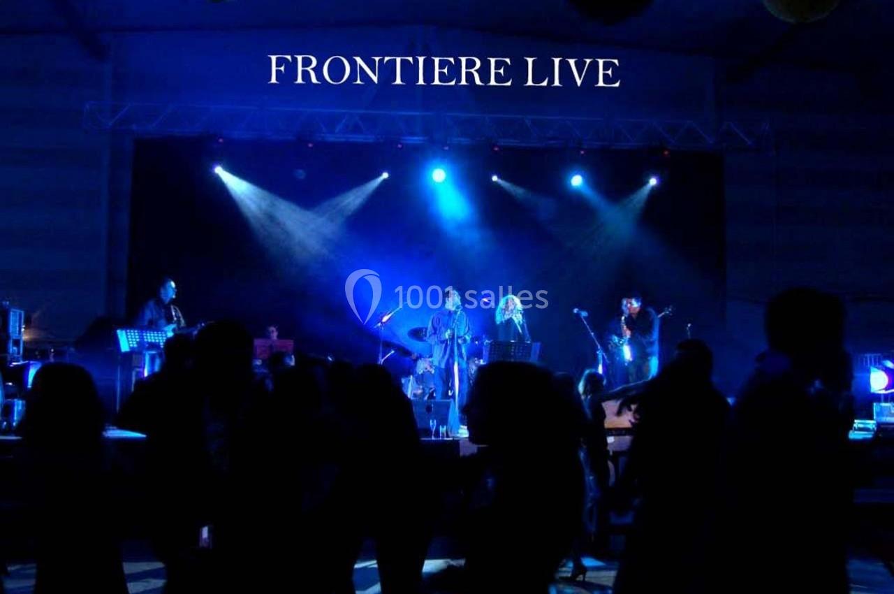 Groupe de musiciens jouant sur scène éclairée de lumières bleues, avec un public en ombre au premier plan.