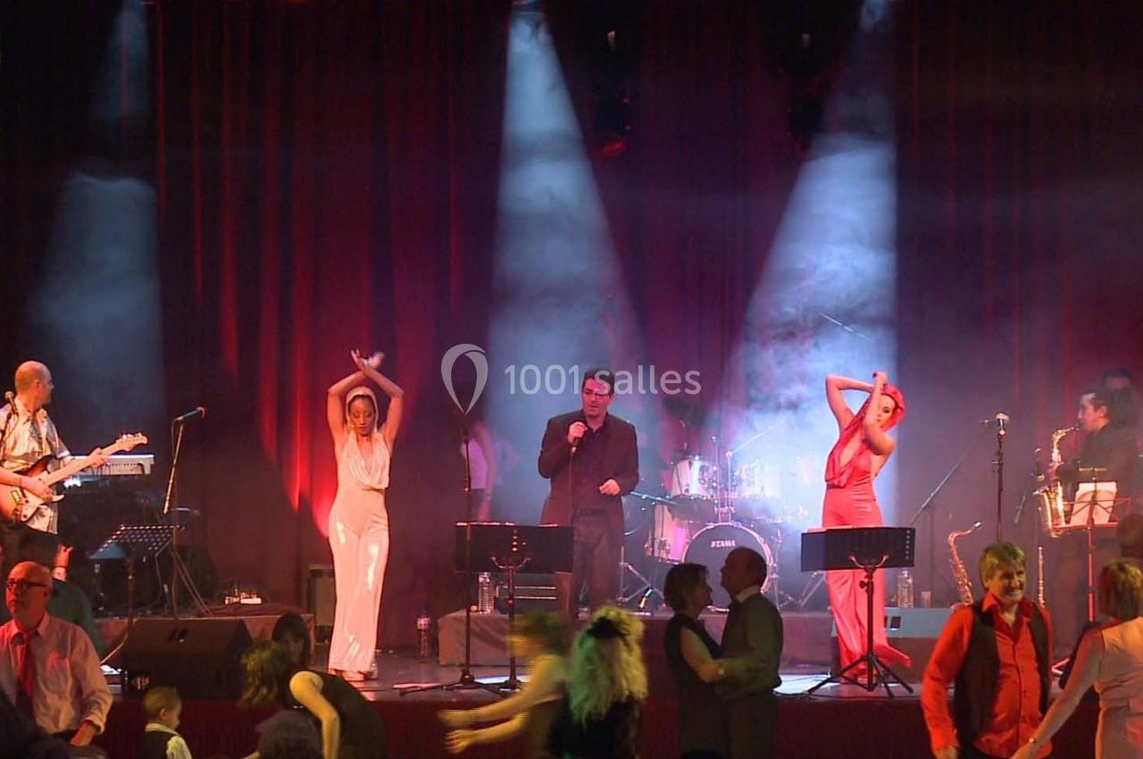 Des musiciens et chanteurs sur scène avec des danseurs au premier plan dans une ambiance lumineuse et festive.