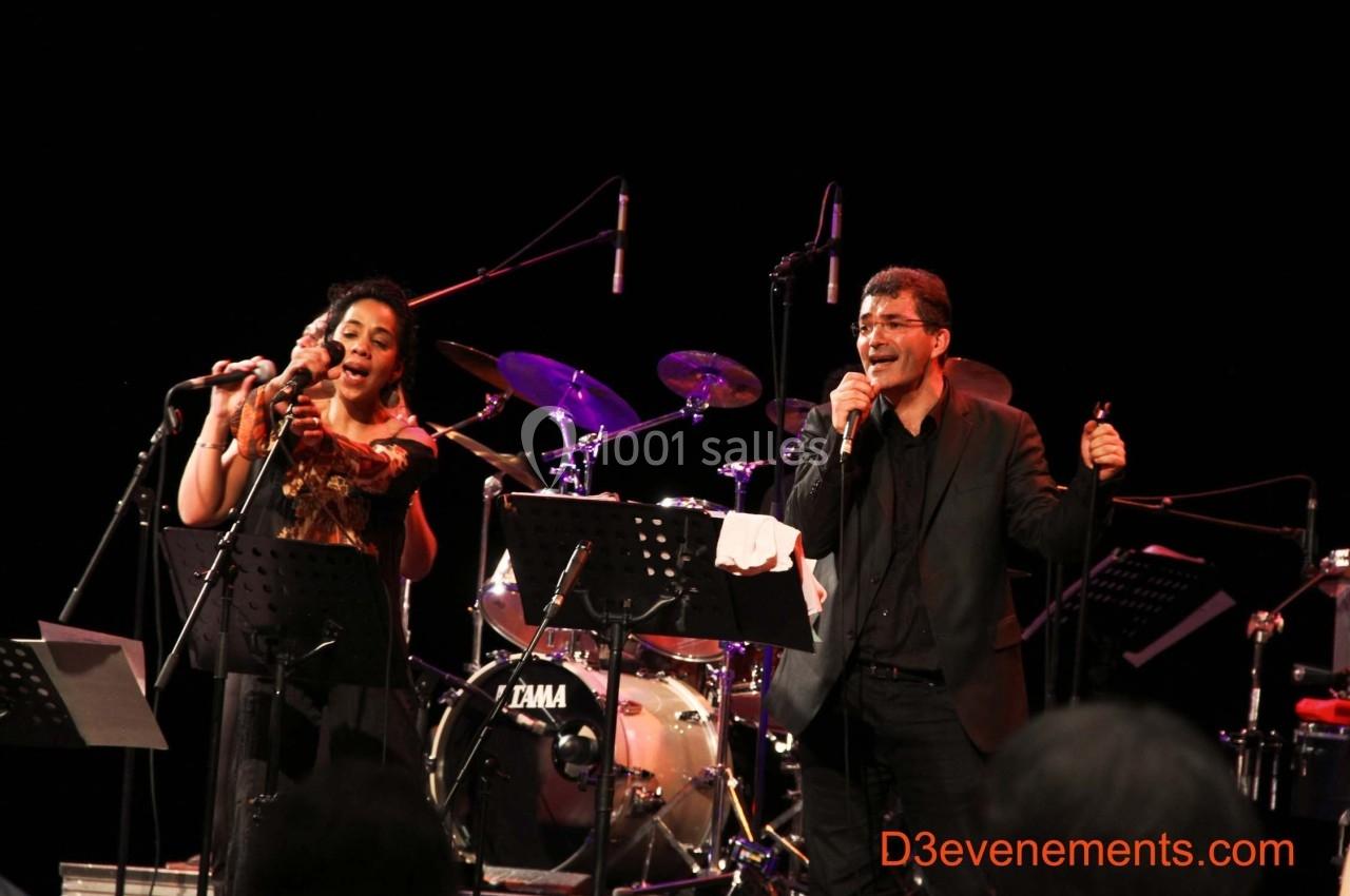 Deux chanteurs sur scène interprétant une chanson, accompagnés de musiciens et d'instruments en arrière-plan.