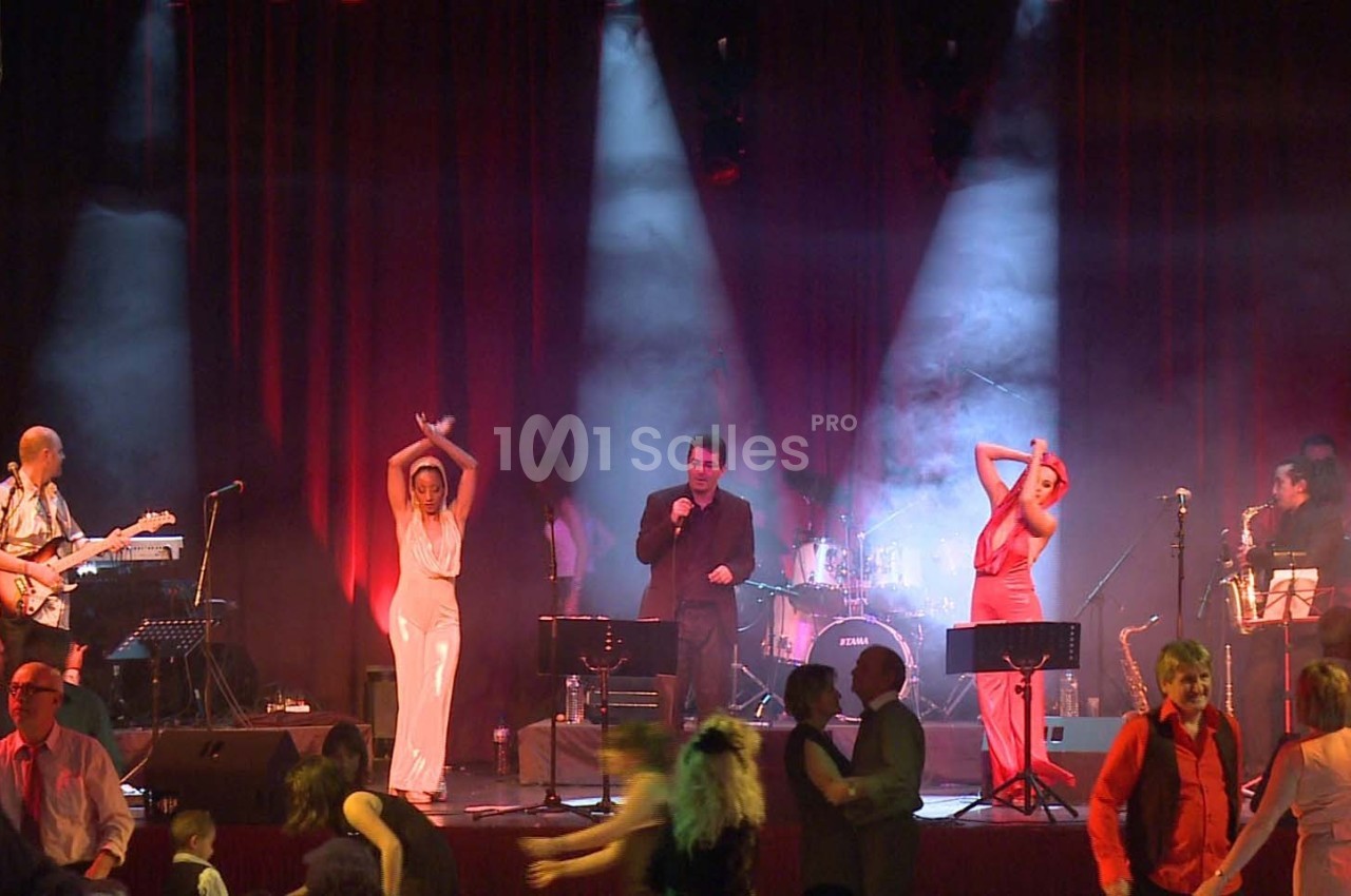 Des musiciens et chanteurs sur scène avec des danseurs au premier plan dans une ambiance lumineuse et festive.