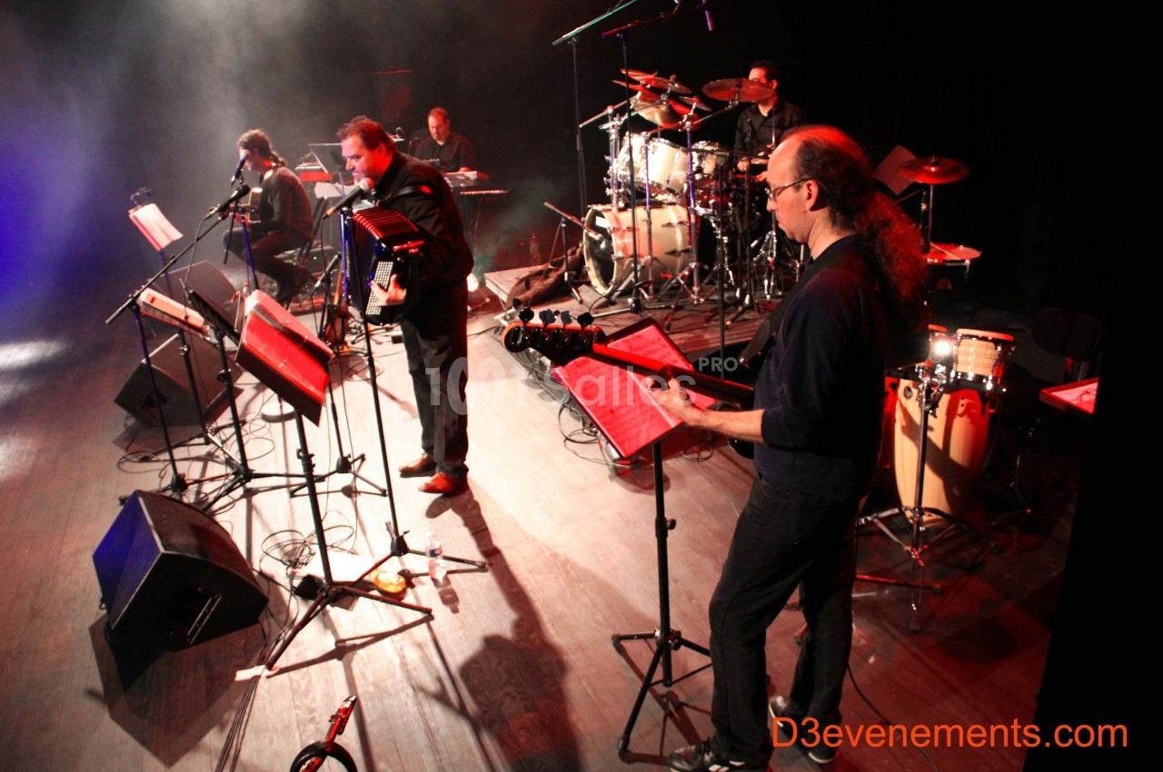 Un groupe de musiciens joue sur scène avec divers instruments, éclairé par des projecteurs.