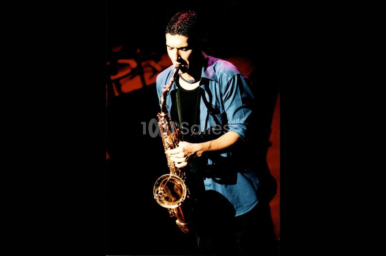 Un musicien joue du saxophone sur une scène sombre, éclairé par une lumière chaude.