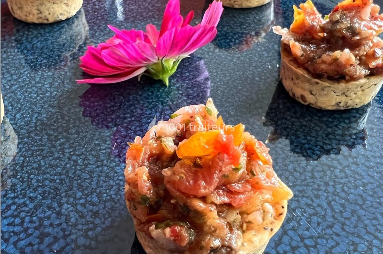 Mini-tartelettes garnies de légumes colorés sur une table texturée, avec une fleur rose en arrière-plan.