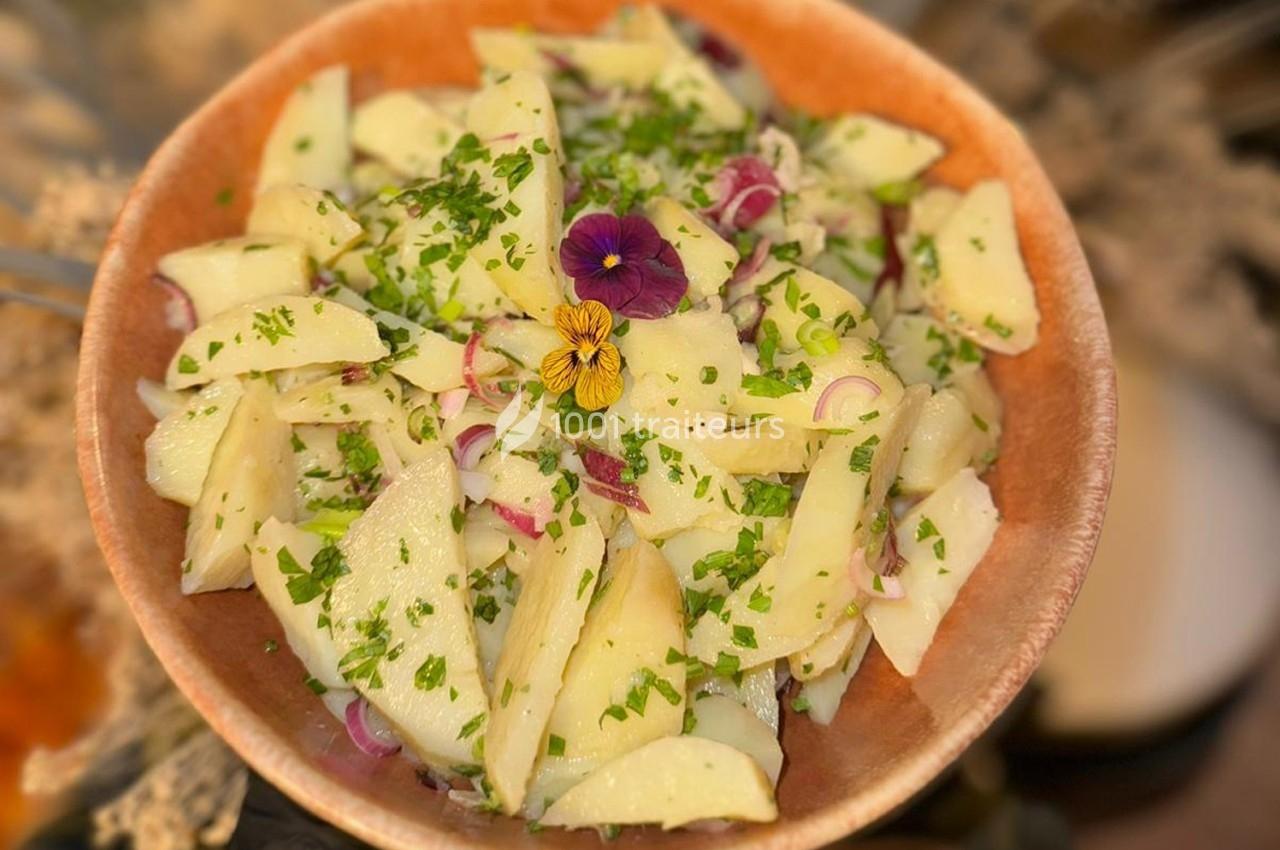Salade de pommes de terre garnie de persil, rondelles d'oignon rouge et fleurs comestibles dans un bol en terre cuite.