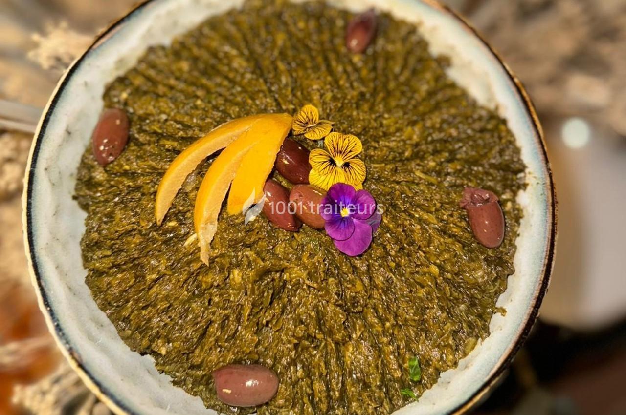 Plat de feuilles de vigne hachées garni d'olives, tranches d'orange et fleurs comestibles, présenté dans une assiette.