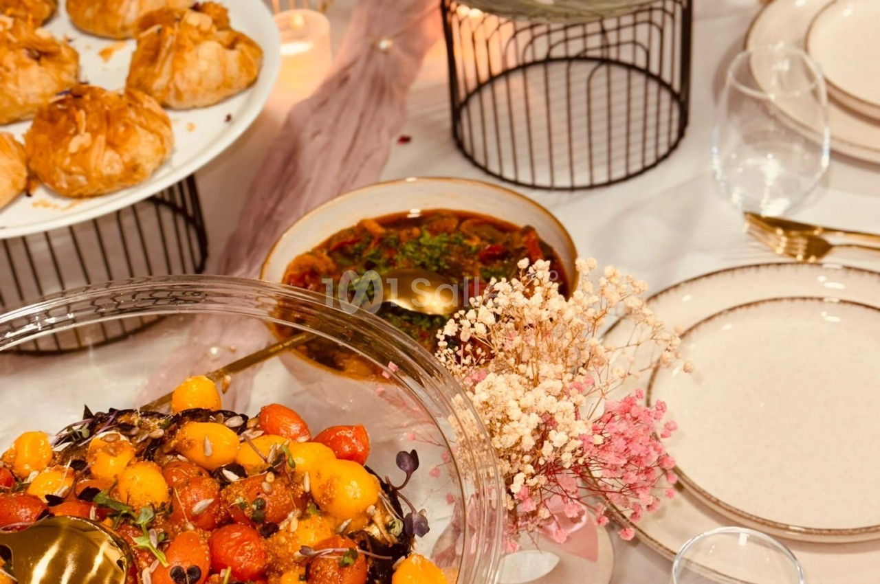Table dressée avec des plats variés, dont une salade de tomates cerises et un plat mijoté, décorée de fleurs séchées.