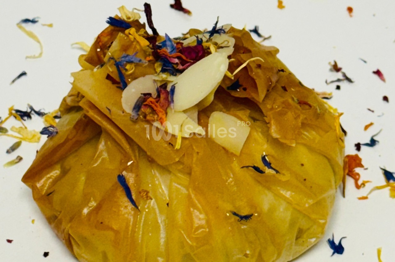 Pochette en tissu jaune contenant des pétales colorés et des morceaux d'amande, posée sur une surface blanche.