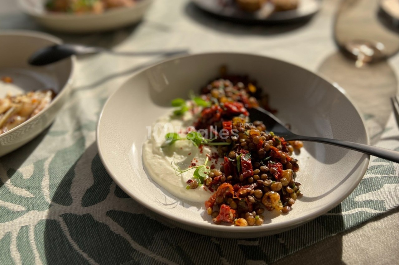 Assiette de lentilles garnies de légumes rôtis et herbes fraîches, accompagnée de yaourt, sur une nappe à motifs.