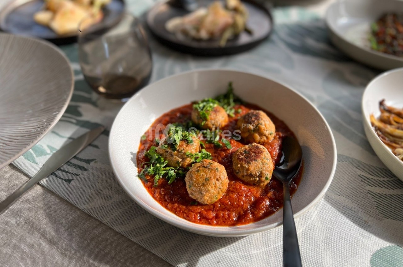 Assiette de boulettes de viande servies sur une sauce tomate, garnies de persil, posée sur une table dressée.