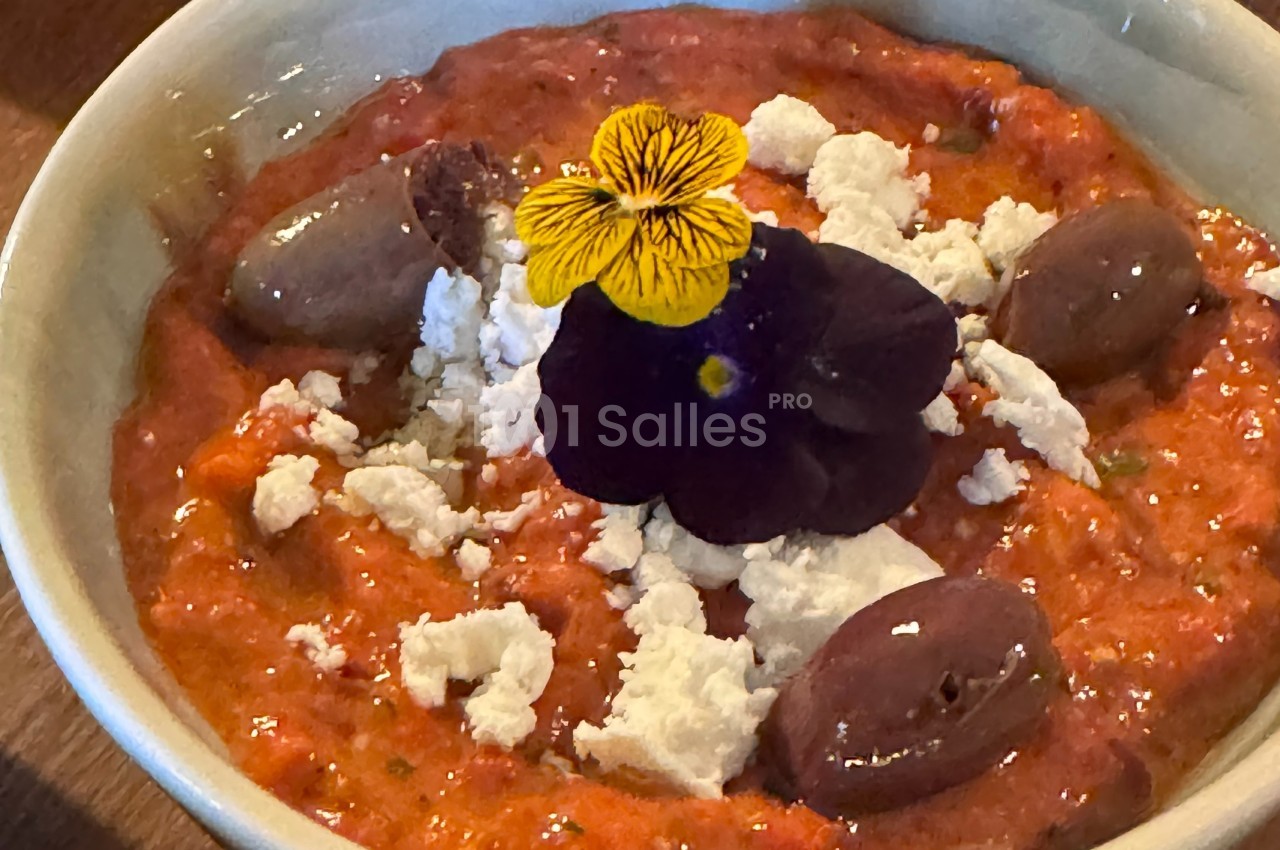 Purée de poivrons rouges garnie de feta émiettée, olives et une fleur comestible violette.