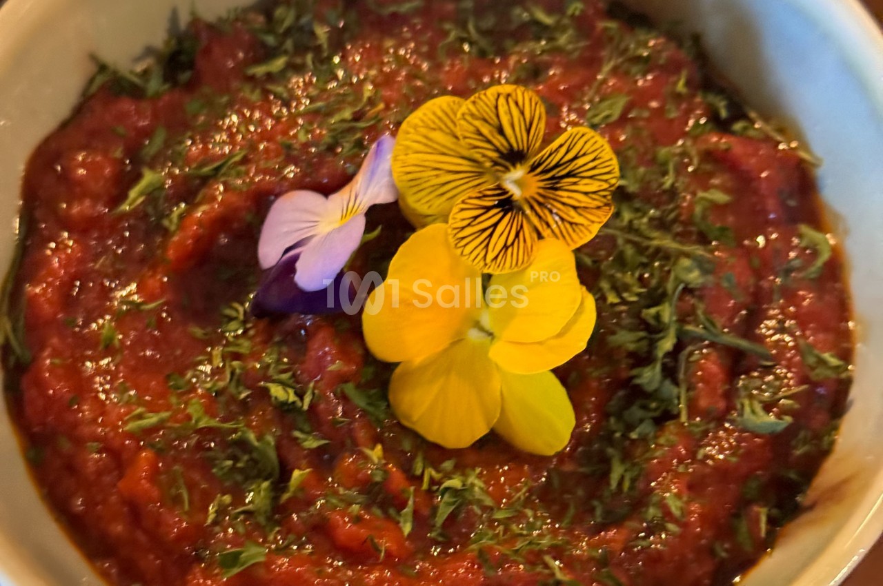 Bol de sauce rouge garnie de fleurs comestibles colorées et de fines herbes hachées.