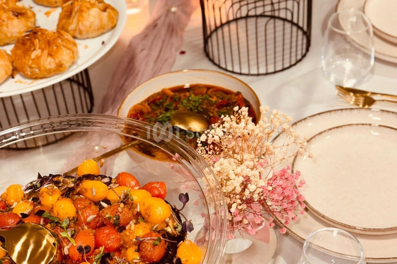 Assortiment de plats colorés sur une table dressée, comprenant une salade de tomates et des pâtisseries.