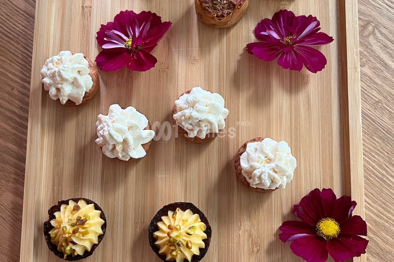 Plateau en bois avec des petits gâteaux décorés de crème et des fleurs roses disposées autour.