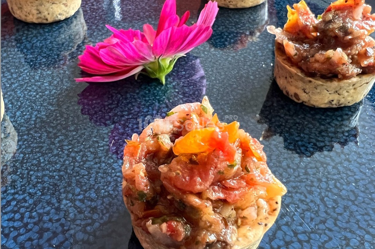Mini-tartelettes garnies de légumes colorés sur une table texturée, avec une fleur rose en arrière-plan.