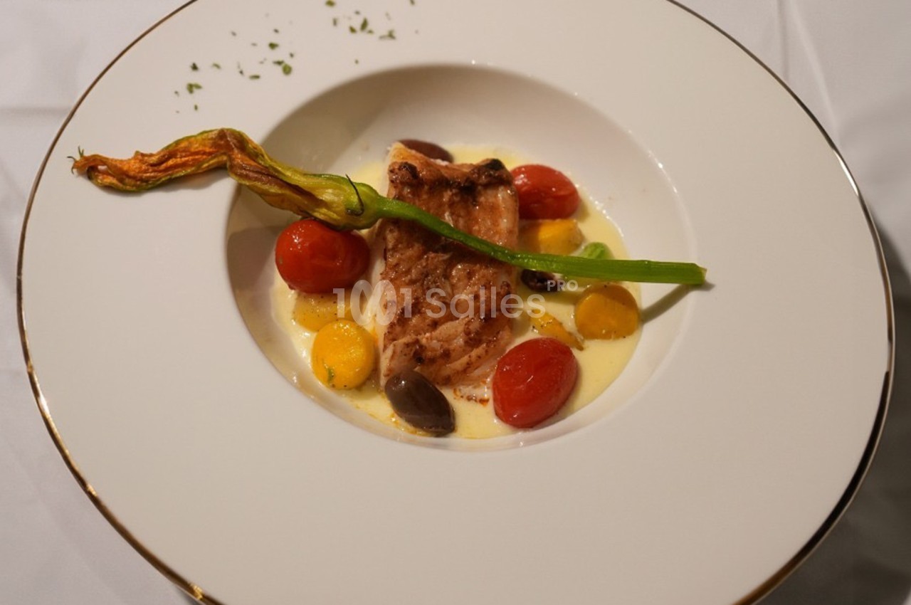 Filet de poisson grillé servi avec des tomates cerises, olives, crème onctueuse et une fleur de courgette en garniture.