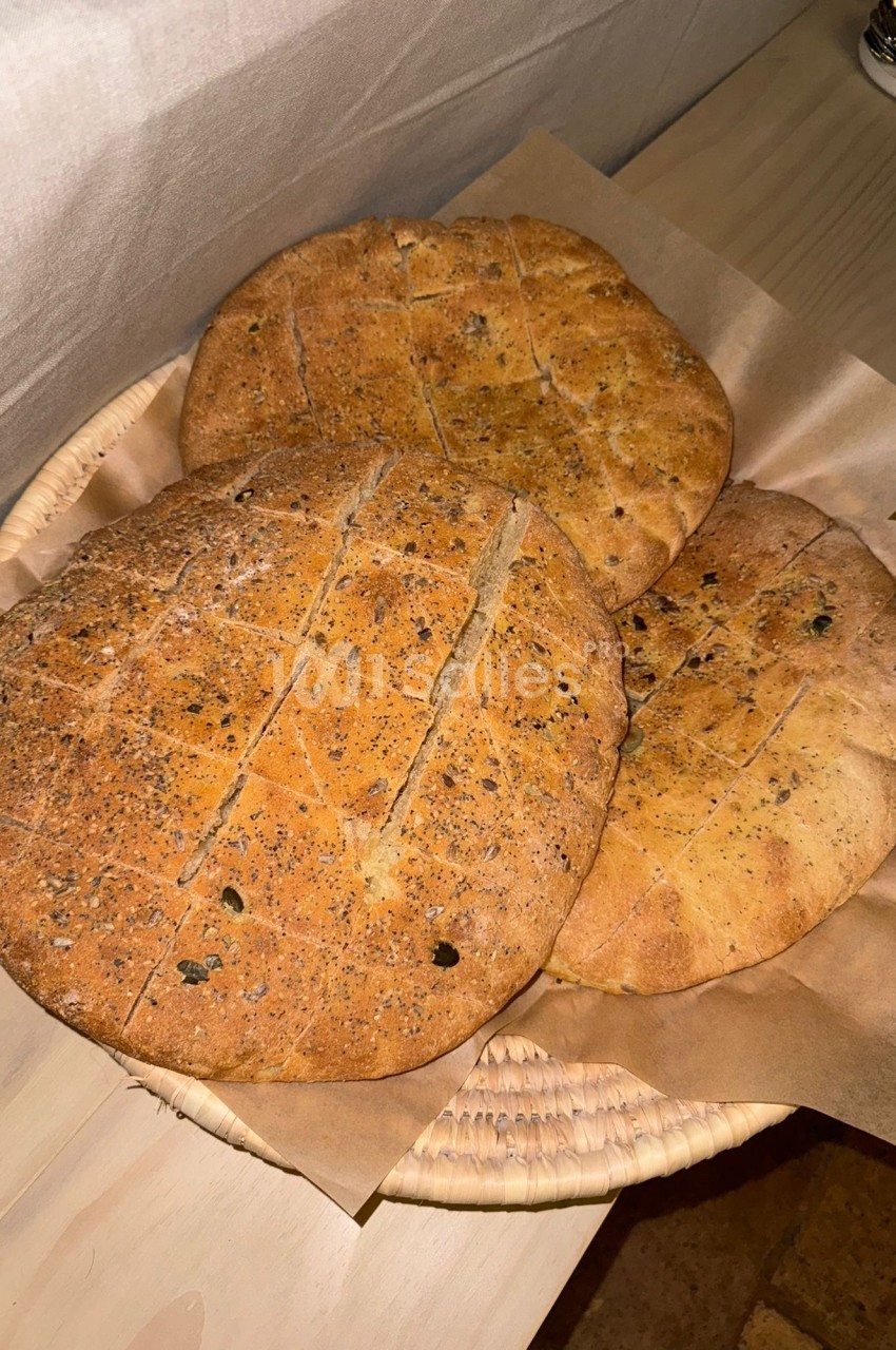 Trois pains ronds dorés, parsemés de graines, disposés dans un panier recouvert de papier brun.