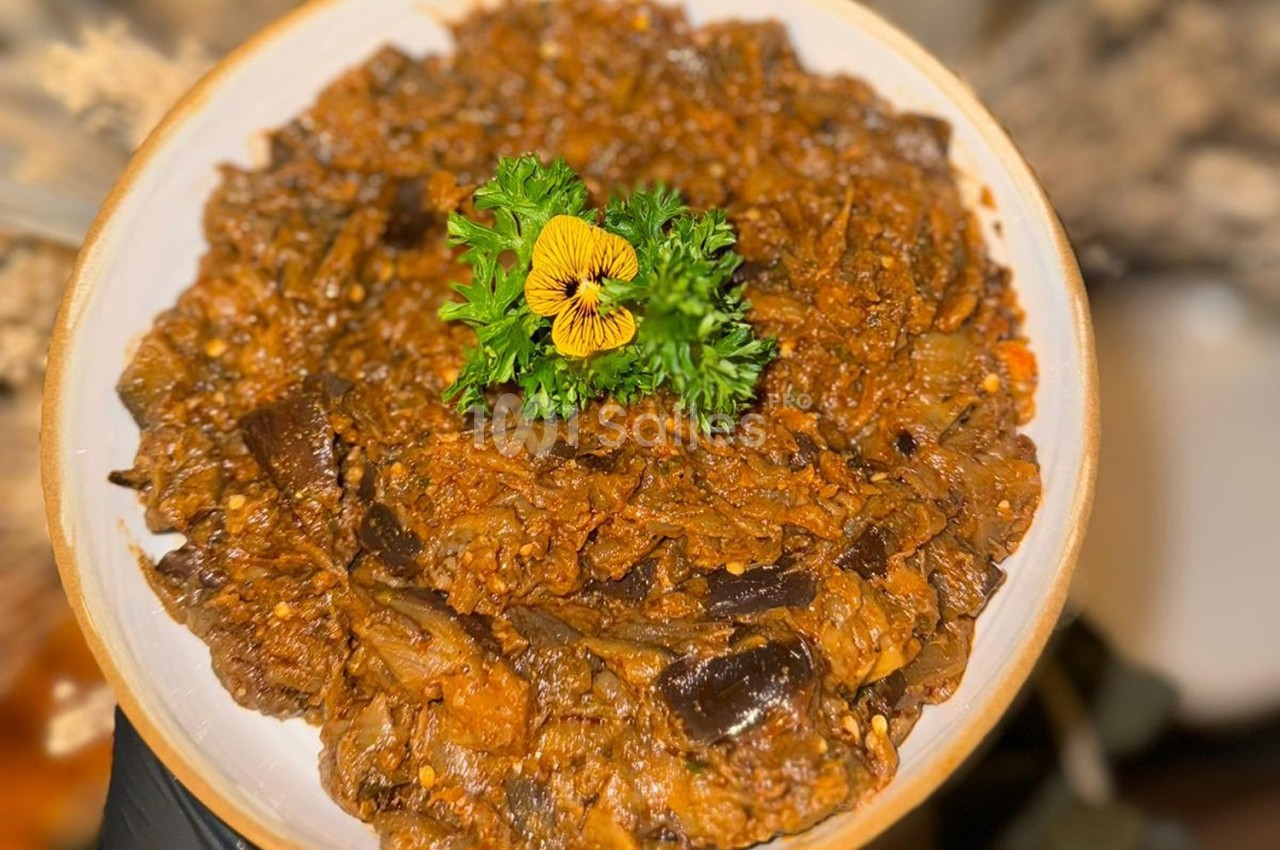 Plat de légumes mijotés avec des aubergines, garni de persil frais et d'une fleur comestible jaune.