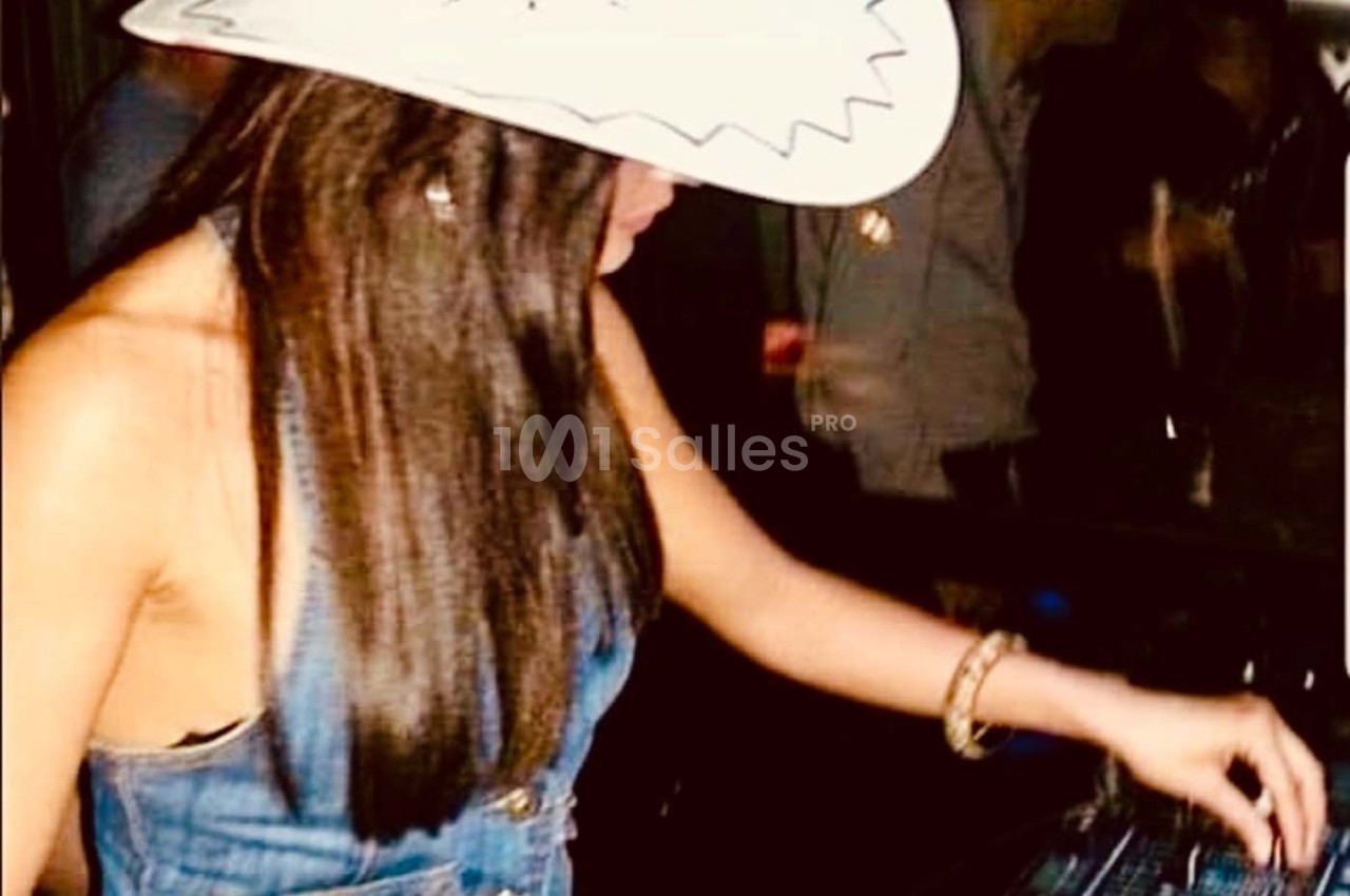 Femme portant un chapeau blanc et une tenue en jean, manipulant des équipements sur une table dans un environnement sombre.