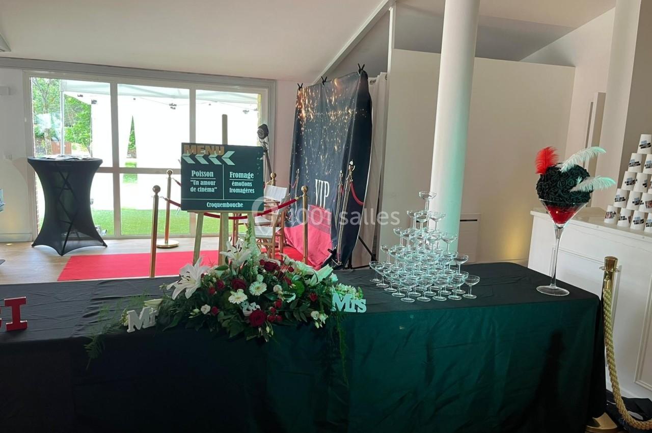 Table décorée avec des fleurs, une pyramide de coupes, et un panneau, dans une salle avec tapis rouge et lumière naturelle.