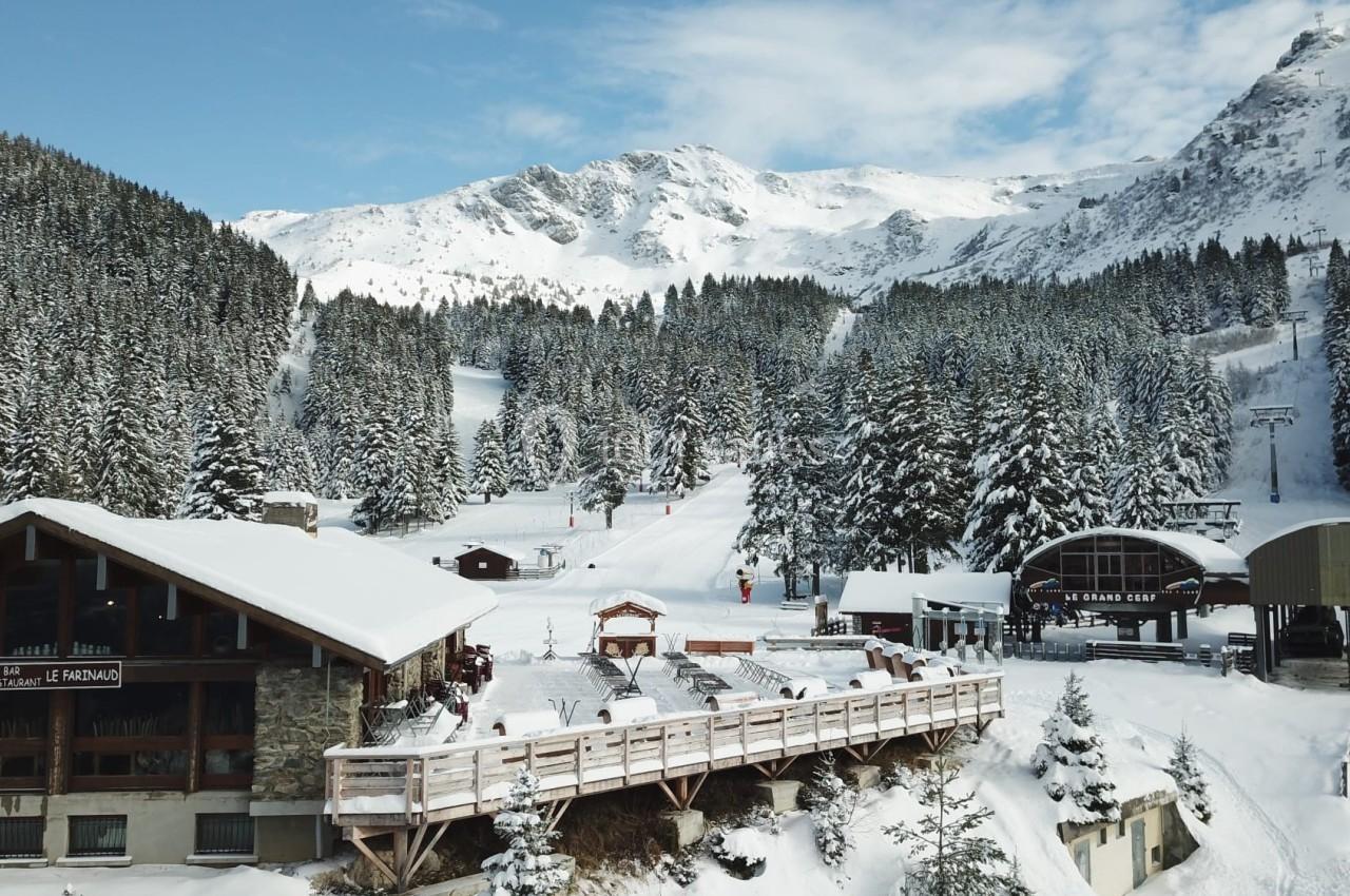 Station de ski enneigée avec chalets, forêt de sapins et remontées mécaniques au pied des montagnes.