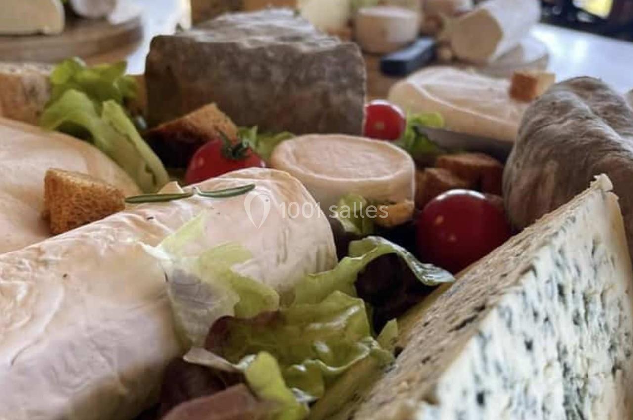 Plateau de fromages variés accompagné de salade, tomates cerises et croûtons, présenté sur une table en bois.